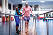 © WavebreakMediaMicro - Female physiotherapist helping disabled senior woman walk with parallel bars in sports center