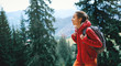 © vitaliymateha - woman hiker with small backpack wearing in red jacket and orange pants walks by trail through pine woods in the Carpathians mountains, Western Ukraine.