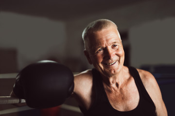 Happy senior boxer man with black gloves in the ring