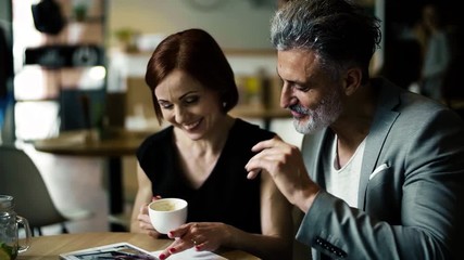 Wall Mural - Man and woman having business meeting in a cafe, using tablet.