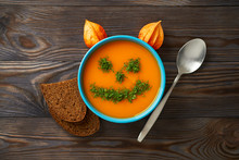 Autumn Cream Soup Garnished With Dill In The Form Of Funny Faces Halloween Pumpkins. Healthy Pumpkin And Carrot Soup Puree In A Blue Bowl On A Wooden Background. Halloween Holiday Concept, Top View.