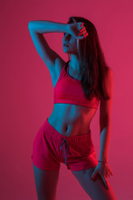 Young Fitness Woman Posing In Sportswear Against Red Light Background.
