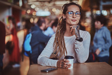 Beautiful Cheerful Girl With Tattooes And Dreadlocks Is Sitting At Food Court While Drinking Coffee.