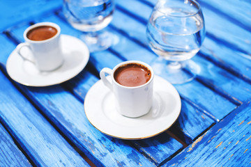 Two cups of coffee and water glass on a blue wooden table.