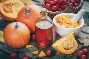 Wall Mural - Pumpkin seeds oil bottle, pumpkins, mortar and basket of  hawthorn berries on wooden table with autumn leaves.