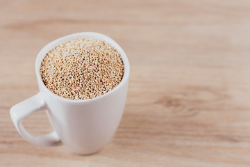 Wall Mural - White cup filled with quinoa grains on wooden background