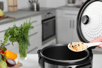 Wall Mural - Woman holding spoon with prepared rice over multi cooker, closeup. Space for text