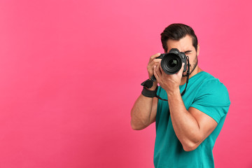 Young professional photographer taking picture on pink background. Space for text