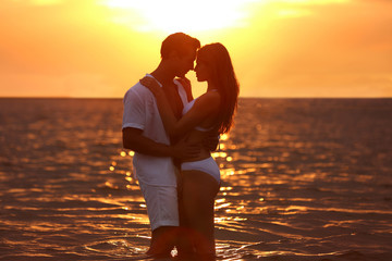 Poster - Happy young couple spending time together on sea beach at sunset