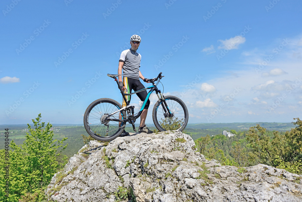 Man on top of a mountain on a bike. - obrazy, fototapety, plakaty 