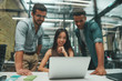 © Friends Stock - Using modern technologies. Group of three young and cheerful employees looking at screen of laptop and smiling while working in modern office