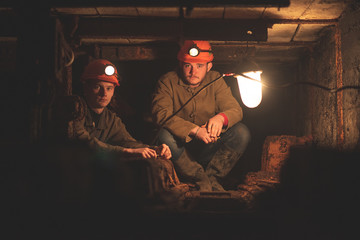 Two young guys in a working uniform and protective helmets, sitting in a low tunnel. Workers of the mine. Miners