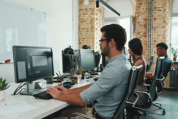 Wall Mural - Focused at work. Side view of young busy employees working on computers while sitting at desk in modern open space