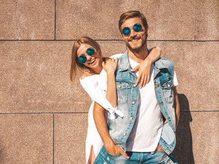 Smiling beautiful girl and her handsome boyfriend. Woman in casual summer dress.Man in jeans clothes.Happy cheerful family.Female having fun on the street near wall.Hugging couple in sunglasses