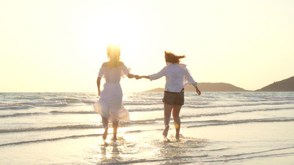 Young Asian lesbian couple running on beach. Beautiful women friends happy relax having fun on beach near sea when sunset in evening. Lifestyle lesbian couple travel on beach concept.