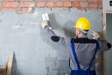 Male in the helmet is plastering the wall