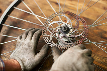 Cropped shot of mechanic working in bicycle repair shop, repairer fixing bike wheel using special tool, wearing protective gloves