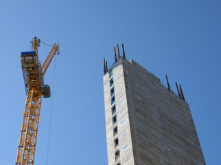 Wall Mural - a yellow tower crane working on a construction site with a tall concrete tower against a bright blue sky