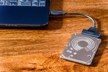 hdd 2.5 internal hard drive disk connected to laptop via sata usb cable on wooden table closeup view