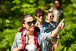 travel, tourism, hike and people concept - woman showing something to group of friends walking with backpacks in forest