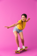 Wall Mural - Image of young happy woman wearing casual clothes smiling and riding skateboard