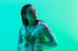 © Drobot Dean - Serious woman posing isolated over blue wall background with neon bright lights dressed in raincoat.