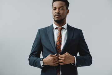 handsome bearded african american businessman touching suit isolated on grey