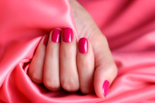 Female hand with pink manicure on a background of pink satin fabric