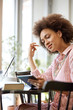 © chika_milan - Attractive mixed race woman in striped pink dress sitting in cafe and using tablet.