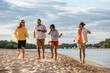 © LIGHTFIELD STUDIOS - cheerful multicultural friends running on sand beach near river