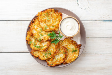 Wall Mural - Potato pancakes or latkes or draniki with sour cream in plate on white wooden table. Top view. Copy space.