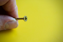 Close up of a crosshead screw held by a human hand on a yellow background