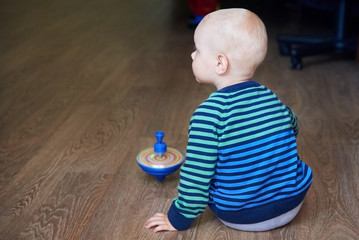 Wall Mural - Cute boy in a striped sweater plays with whirligig on the floor, back view