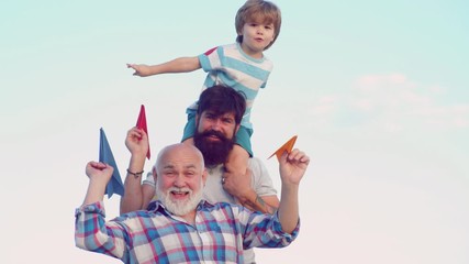 Wall Mural - Happy child with father and grandfather playing with toy paper airplane against summer sky background. Grandfather playtime. Cute son with dad and father playing outdoor.