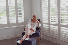 Active Senior Woman With Hand On Chin Sitting On Chair In A Comfortable Home
