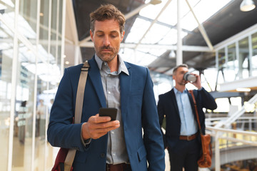 Wall Mural - Businessman using mobile phone while walking in the corridor