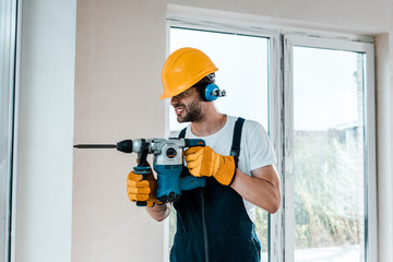 Wall Mural - handyman in uniform and yellow gloves using hammer drill