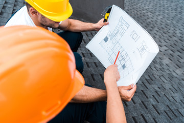 Wall Mural - selective focus of architect in helmet holding pencil near blueprint and coworker