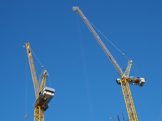 Wall Mural - two tall yellow tower cranes working on a construction site against a blue sky