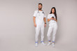 © NASTYA PALEHINA - two young stylish doctors, male and female nurses, in white casual costumes are standing on a white wall background. he is looking away, she is looking to the mobile phone. medical concept. free space