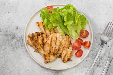 Grilled chicken fillet with greens on a white plate. Gray background