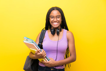 African American teenager student girl with long braided hair over isolated yellow wall applauding