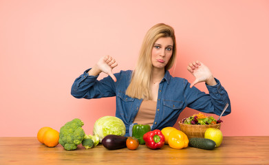 Wall Mural - Young blonde woman with many vegetables showing thumb down