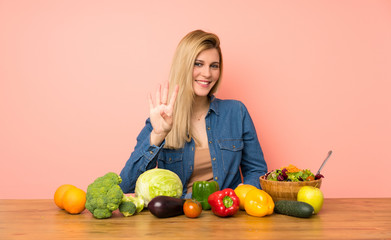 Wall Mural - Young blonde woman with many vegetables happy and counting four with fingers