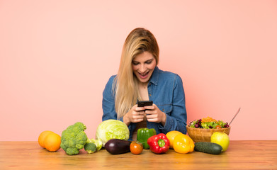 Wall Mural - Young blonde woman with many vegetables surprised and sending a message