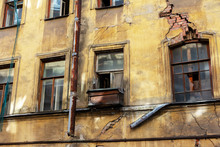 Collapsing Facade Of An Old Building With Broken Windows And Crack In A Brick Wall