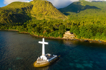 Wall Mural - Aerial view of a large memorial cross marking a sunken cemetery in golden evening sunlight (Camiguin, Philippines)