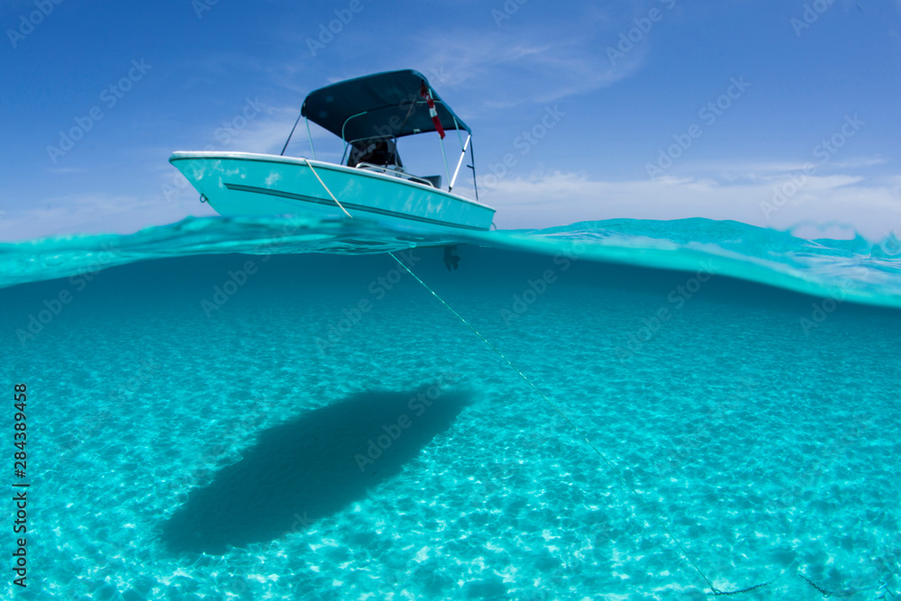 A boat is anchored in the clear blue tropical waters off Staniel Cay, Exuma, Bahamas - obrazy, fototapety, plakaty 