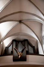 Wels, Upper Austria, Austria - A Statue Of An Angel Is In Front Of A Pipe Organ's Pipes In A Church.