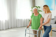 Caretaker helping elderly woman with walking frame indoors